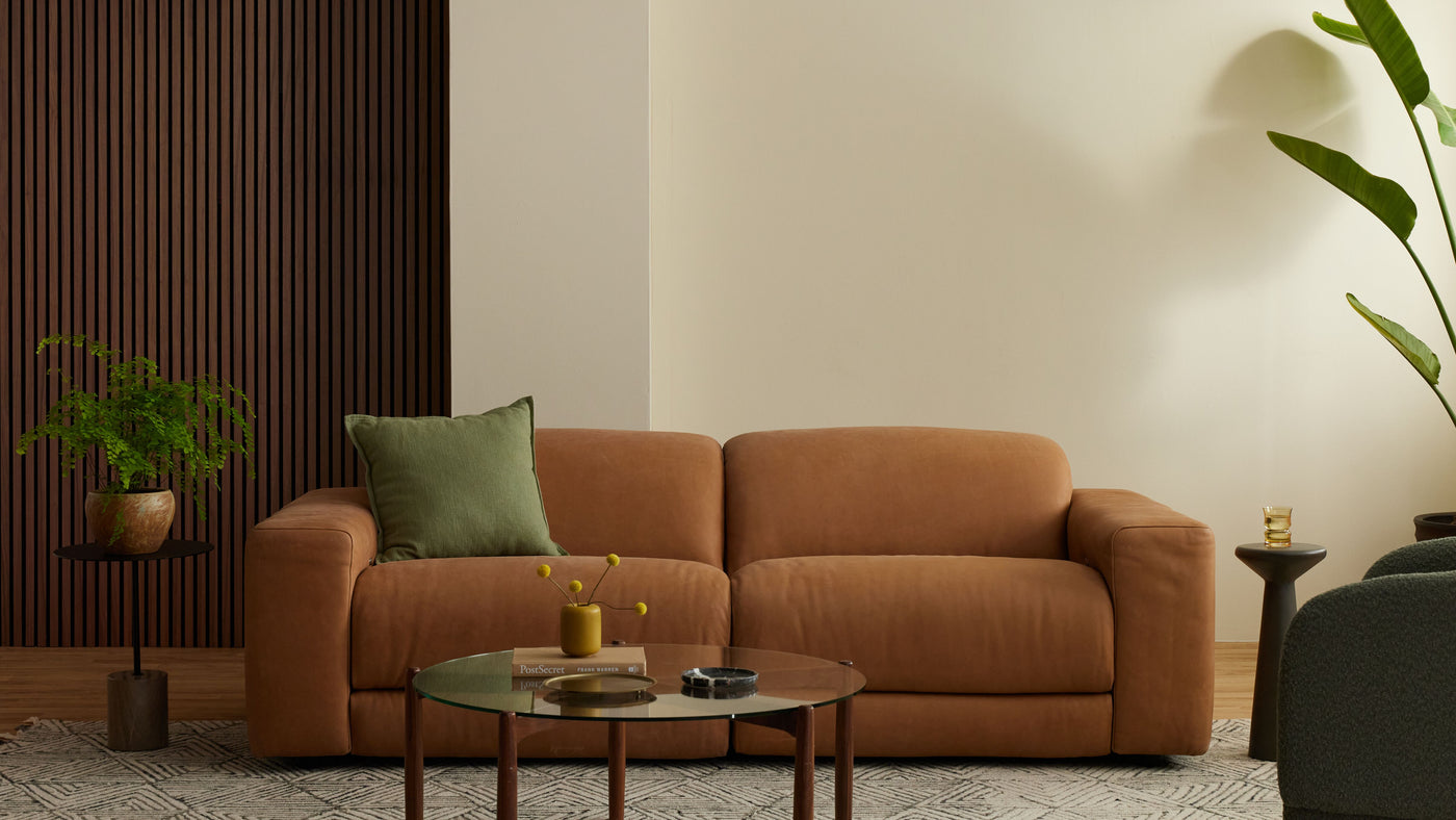 Brown sofa in a living room with a coffee table, plants and dark coloured smoked oak wall panelling