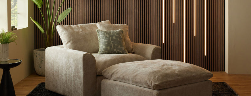 Beige armchair with decorative pillows in a modern living room setting with walnut acoustic wood wall panelling covering most of the wall.